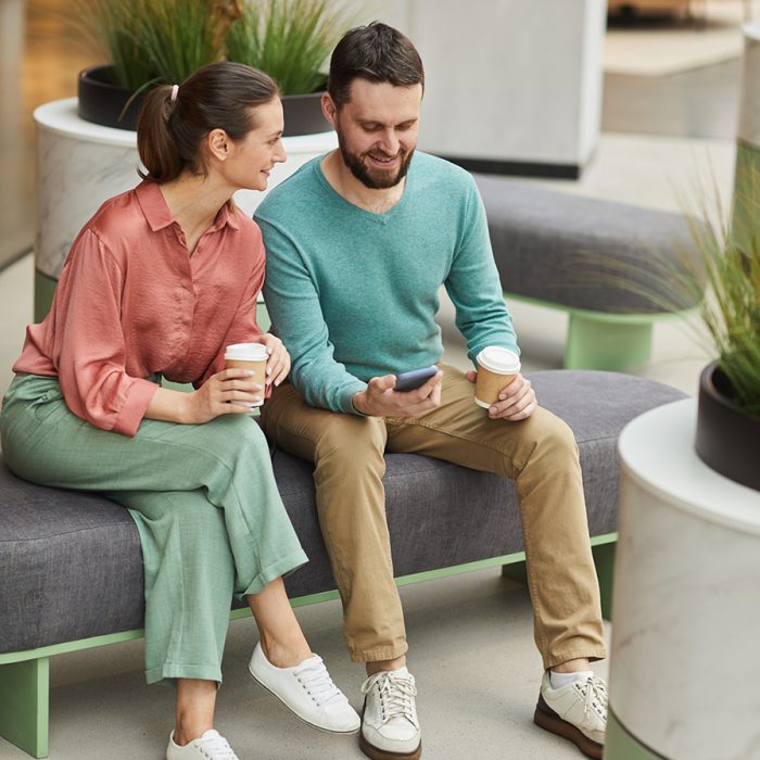 Young couple drinking coffee and using mobile phone while sitting on sofa in the mall
