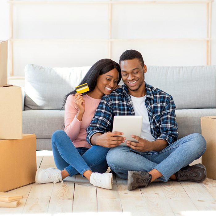 Online shopping concept. Happy black couple with tablet computer and credit card buying household goods on web. Young African American family purchasing home decor on internet