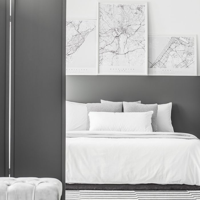 Black screen in minimal hotel room interior with maps above bed next to a clock and table